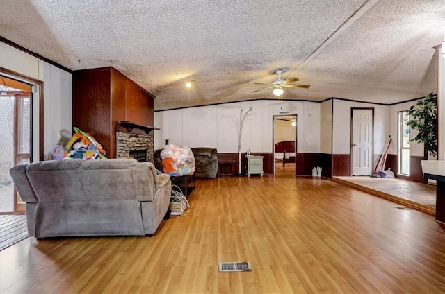 living room with a fireplace, vaulted ceiling, ceiling fan, a textured ceiling, and light hardwood / wood-style flooring