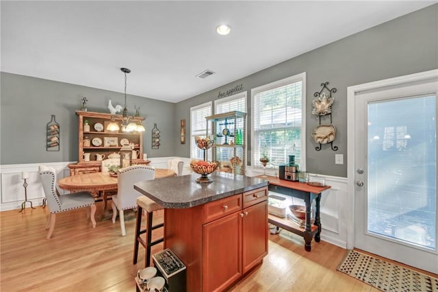 kitchen with a wainscoted wall, light wood finished floors, dark countertops, visible vents, and a chandelier