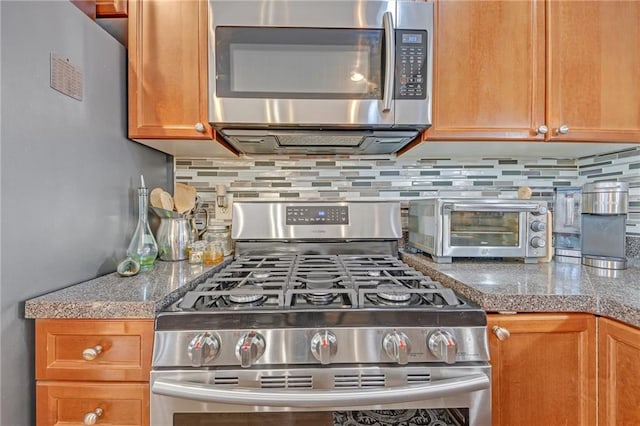 kitchen with appliances with stainless steel finishes, brown cabinetry, decorative backsplash, and a toaster