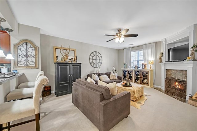 living area with a lit fireplace, baseboards, ceiling fan, and light colored carpet