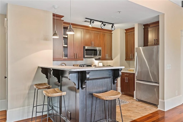kitchen featuring decorative light fixtures, appliances with stainless steel finishes, brown cabinetry, and a kitchen bar