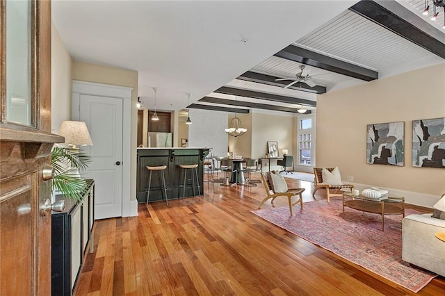living area featuring beamed ceiling, ceiling fan with notable chandelier, and wood finished floors