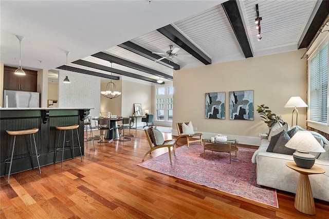 living room with light wood-style floors, beamed ceiling, ceiling fan with notable chandelier, and a wealth of natural light