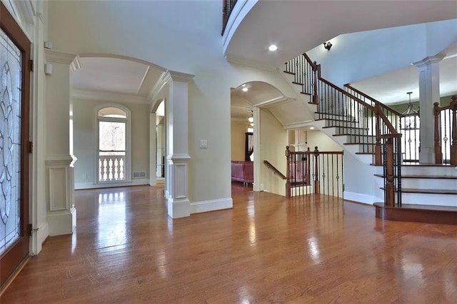 foyer with arched walkways, decorative columns, visible vents, wood finished floors, and baseboards