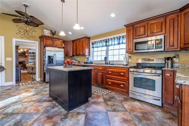 kitchen featuring stainless steel appliances, vaulted ceiling, a brick fireplace, light stone countertops, and pendant lighting