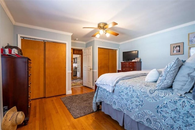 bedroom with hardwood / wood-style flooring, ceiling fan, ornamental molding, and two closets