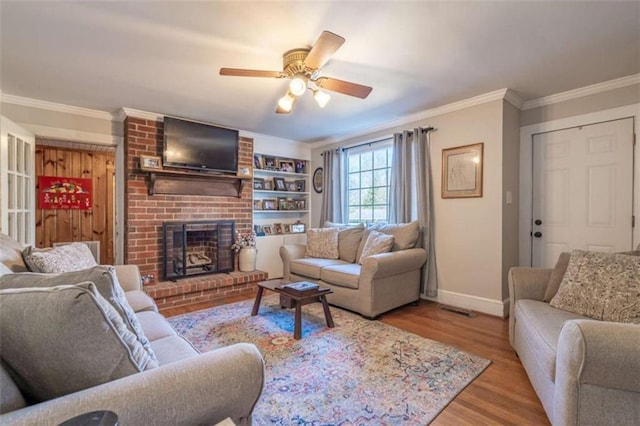 living room featuring ornamental molding, a ceiling fan, a brick fireplace, wood finished floors, and baseboards