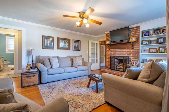 living room featuring a fireplace, ornamental molding, a ceiling fan, wood finished floors, and baseboards