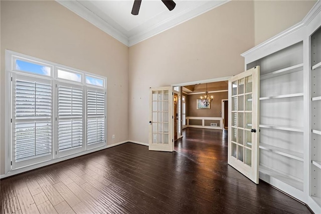 empty room with french doors, ceiling fan with notable chandelier, a high ceiling, crown molding, and dark wood-type flooring