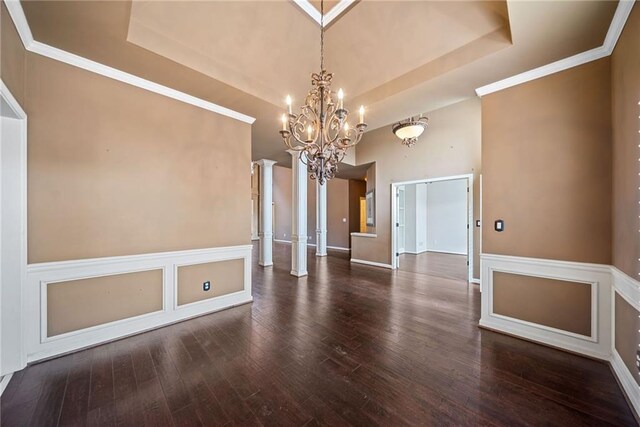 spare room with dark hardwood / wood-style flooring, an inviting chandelier, decorative columns, and a tray ceiling