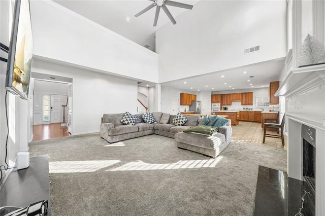 living room with a fireplace, light carpet, a towering ceiling, and ceiling fan