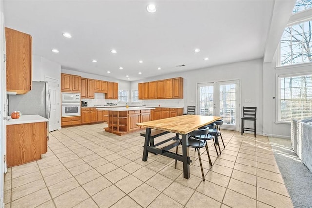 kitchen with light tile patterned floors, white appliances, a kitchen island, and a healthy amount of sunlight