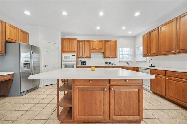 kitchen featuring decorative backsplash, white appliances, sink, light tile patterned floors, and a center island