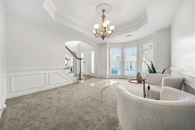 living room featuring a notable chandelier, carpet floors, ornamental molding, and a tray ceiling