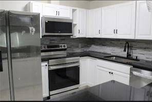 kitchen featuring white cabinetry, backsplash, dark countertops, appliances with stainless steel finishes, and a sink