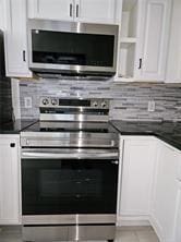 kitchen with appliances with stainless steel finishes, dark countertops, white cabinets, and backsplash