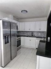 kitchen with dark countertops, decorative backsplash, appliances with stainless steel finishes, white cabinetry, and a sink