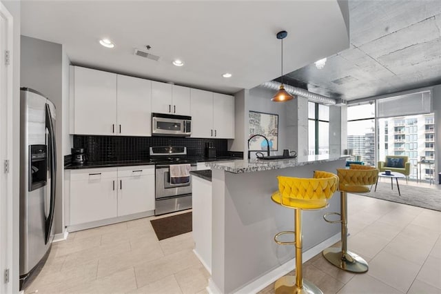 kitchen featuring visible vents, stainless steel appliances, white cabinetry, decorative light fixtures, and backsplash