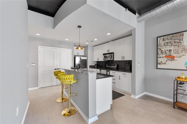 kitchen with backsplash, a center island with sink, appliances with stainless steel finishes, a kitchen breakfast bar, and white cabinetry