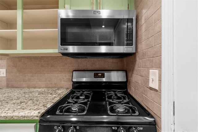 kitchen with tasteful backsplash, light stone countertops, black range, and green cabinetry