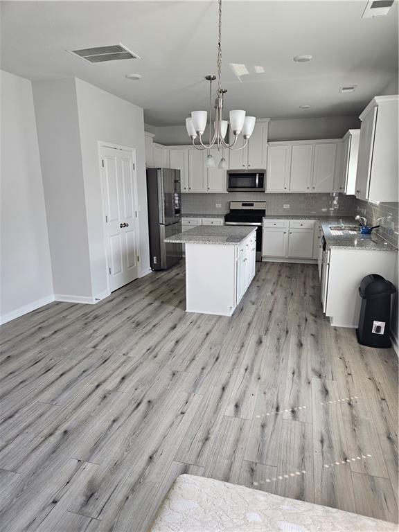 kitchen with appliances with stainless steel finishes, hanging light fixtures, tasteful backsplash, white cabinets, and a kitchen island