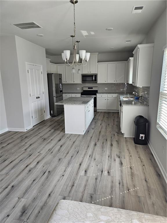 kitchen featuring pendant lighting, appliances with stainless steel finishes, backsplash, a center island, and white cabinets