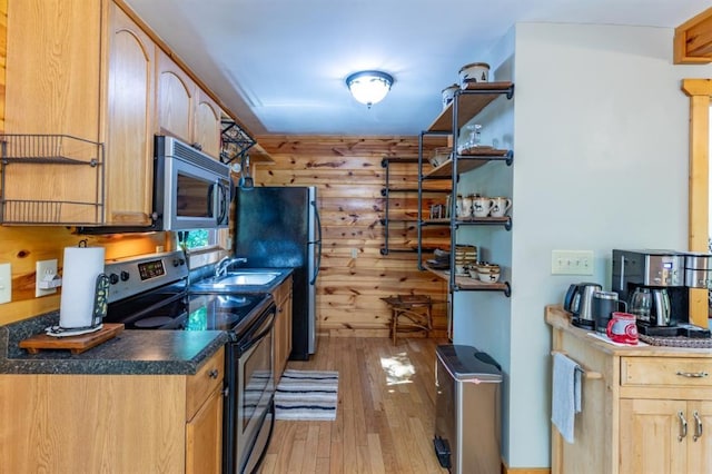 kitchen featuring sink, wooden walls, light wood-type flooring, light brown cabinetry, and appliances with stainless steel finishes