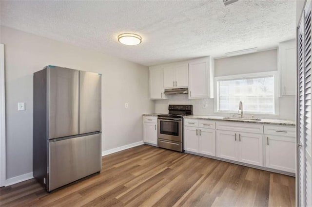 5119 NE Worsham St, Covington, GA 30014 - kitchen featuring appliances with stainless steel finishes, under cabinet range hood, wood finished floors, white cabinets, and a textured ceiling