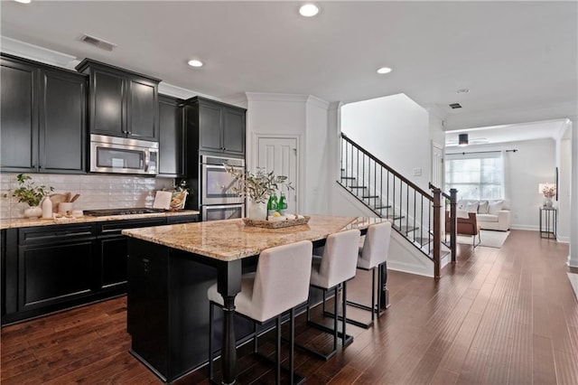 kitchen featuring a kitchen bar, appliances with stainless steel finishes, decorative backsplash, dark wood-type flooring, and a center island