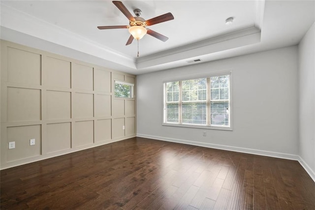 empty room featuring a tray ceiling, dark hardwood / wood-style floors, crown molding, and ceiling fan