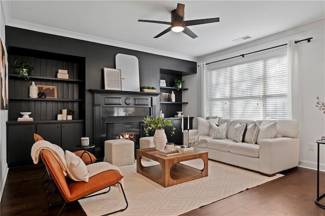 living room with dark hardwood / wood-style flooring, built in features, ceiling fan, and ornamental molding