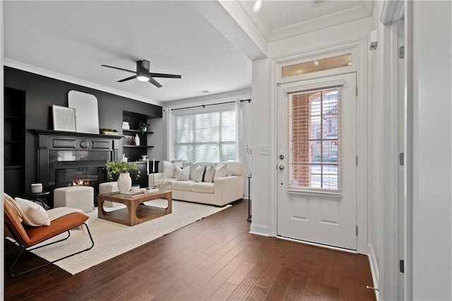 living room with built in shelves, dark hardwood / wood-style flooring, ceiling fan, and crown molding