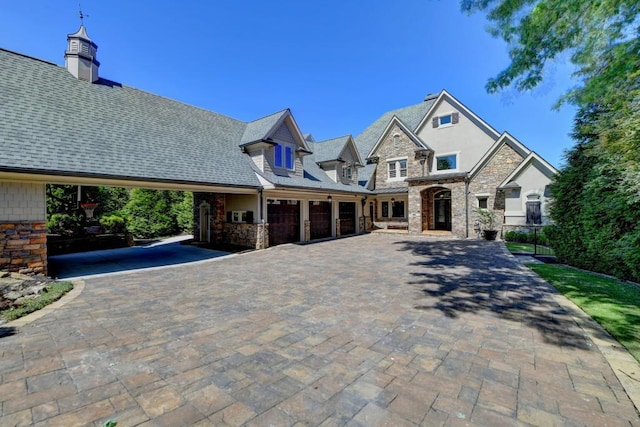 french country home with a garage, decorative driveway, stucco siding, and stone siding