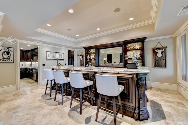 bar with stone finish flooring, wet bar, a tray ceiling, and ornamental molding