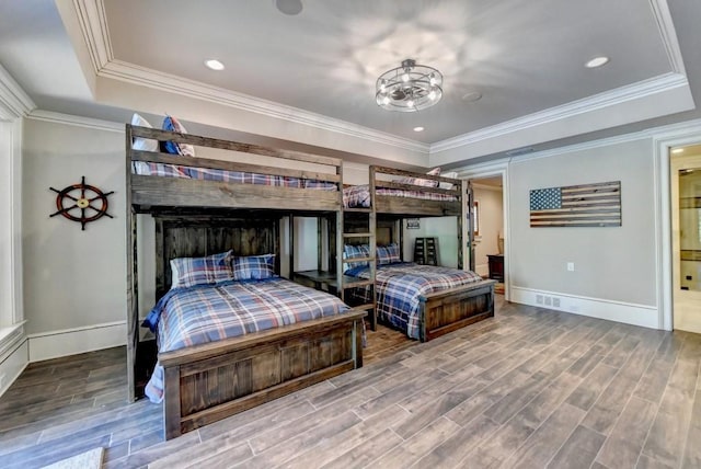 bedroom with baseboards, ornamental molding, wood finished floors, and a tray ceiling