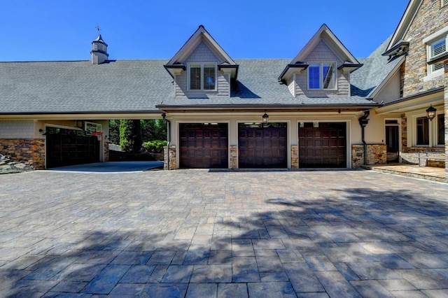 exterior space featuring roof with shingles, an attached garage, decorative driveway, and stone siding