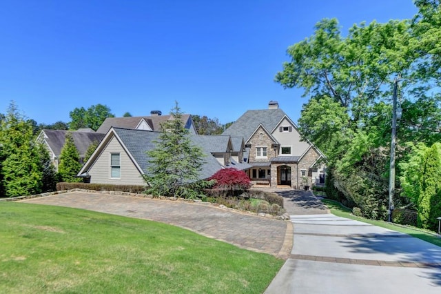 view of front of house with a chimney, driveway, a front yard, and stone siding