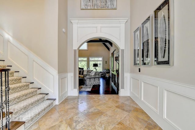 entrance foyer with a high ceiling, a decorative wall, arched walkways, stone tile floors, and stairway