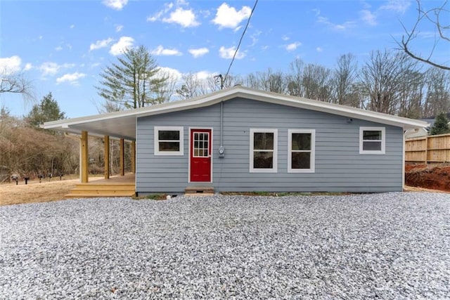 view of front facade featuring gravel driveway, a carport, and fence