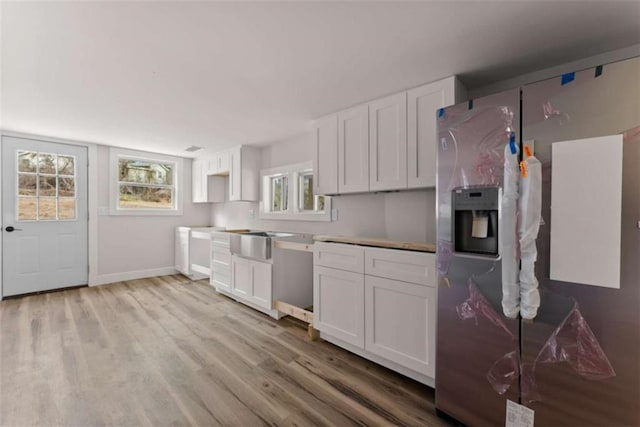 kitchen featuring baseboards, light wood-style flooring, stainless steel refrigerator with ice dispenser, white cabinetry, and a sink