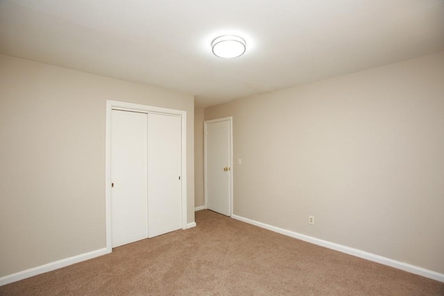 unfurnished bedroom featuring baseboards, a closet, and light carpet