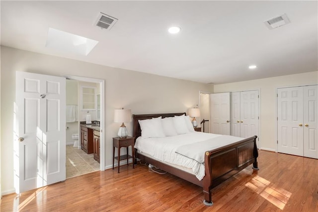 bedroom with multiple closets, light wood-type flooring, and ensuite bath