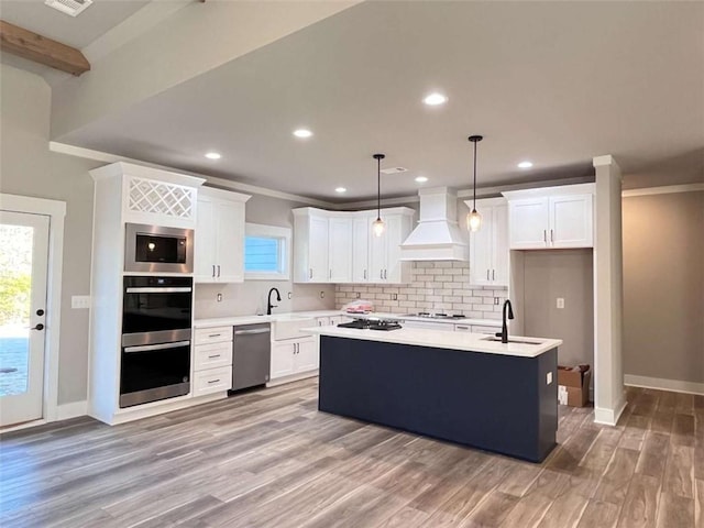 kitchen with tasteful backsplash, appliances with stainless steel finishes, light countertops, premium range hood, and a sink