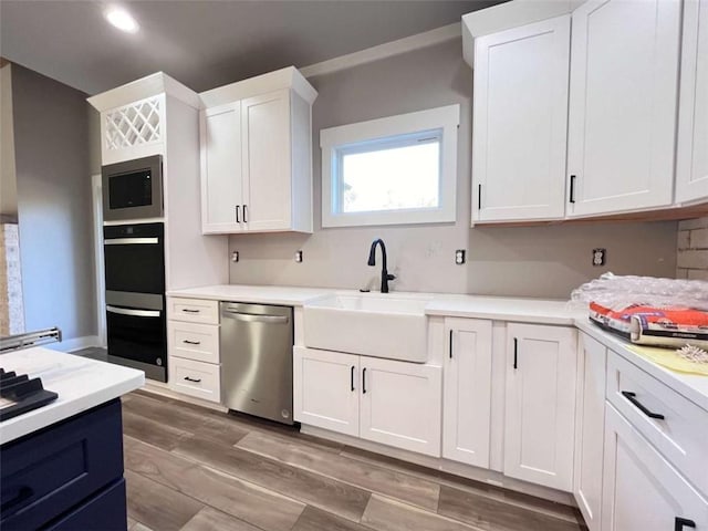 kitchen featuring stainless steel appliances, light countertops, white cabinets, a sink, and light wood-type flooring