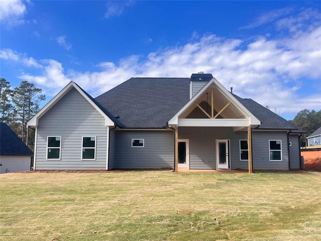 back of property featuring roof with shingles, a lawn, and a chimney