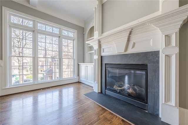 unfurnished living room with a high end fireplace, visible vents, crown molding, and wood finished floors