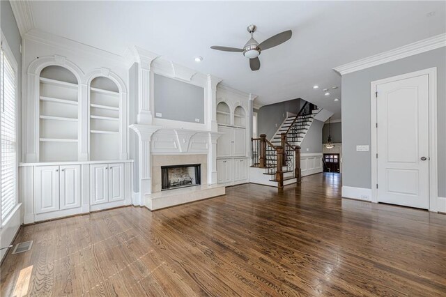 unfurnished living room with a premium fireplace, built in shelves, wood finished floors, and stairway