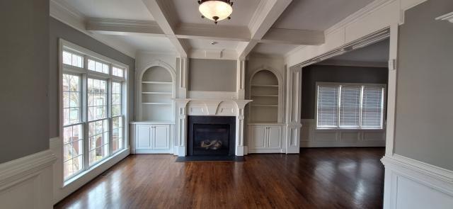 unfurnished living room featuring beam ceiling, plenty of natural light, dark wood finished floors, and built in shelves