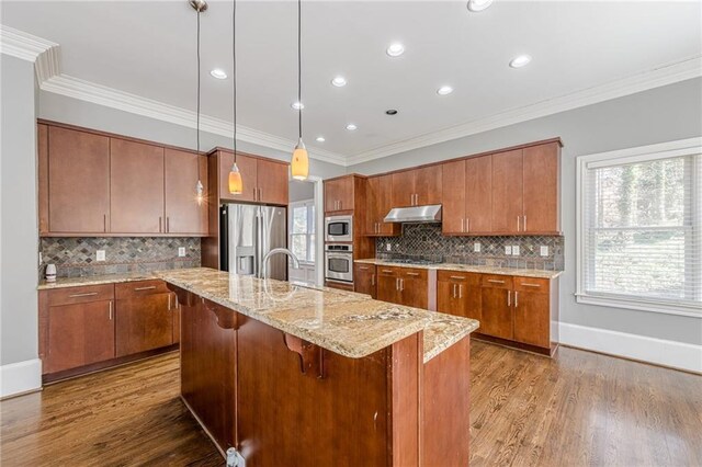 kitchen featuring dark wood-style floors, brown cabinets, under cabinet range hood, and stainless steel appliances