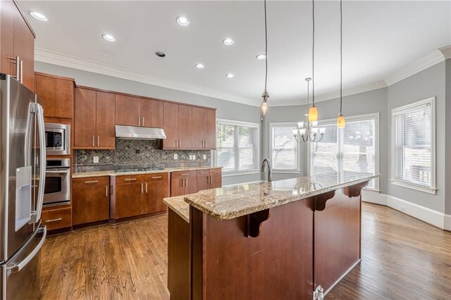 kitchen with under cabinet range hood, decorative backsplash, brown cabinets, and appliances with stainless steel finishes